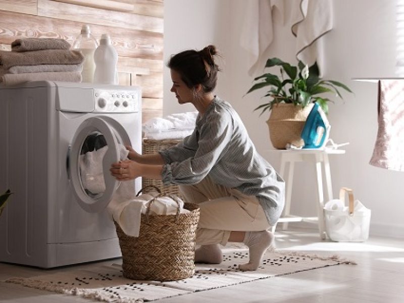 Young,Woman,Taking,Laundry,Out,Of,Washing,Machine,At,Home